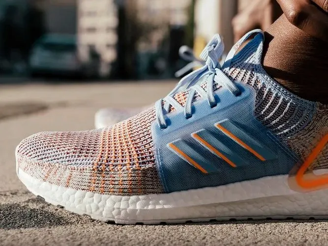 Close detail of a pale blue and orange Ultraboost 19, the three stripes running down the midfoot