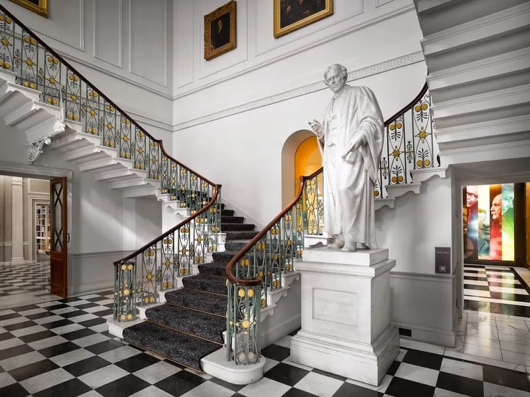 A marble statue on a plinth beside the Ri's sweeping entrance staircase and chequerboard floor